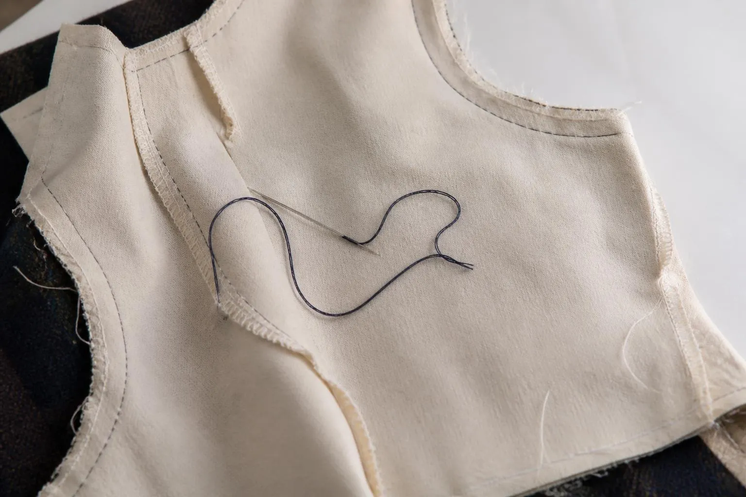 un vêtement en cours de couture, l'envers du tissu visible, aiguille et fil posés dessus